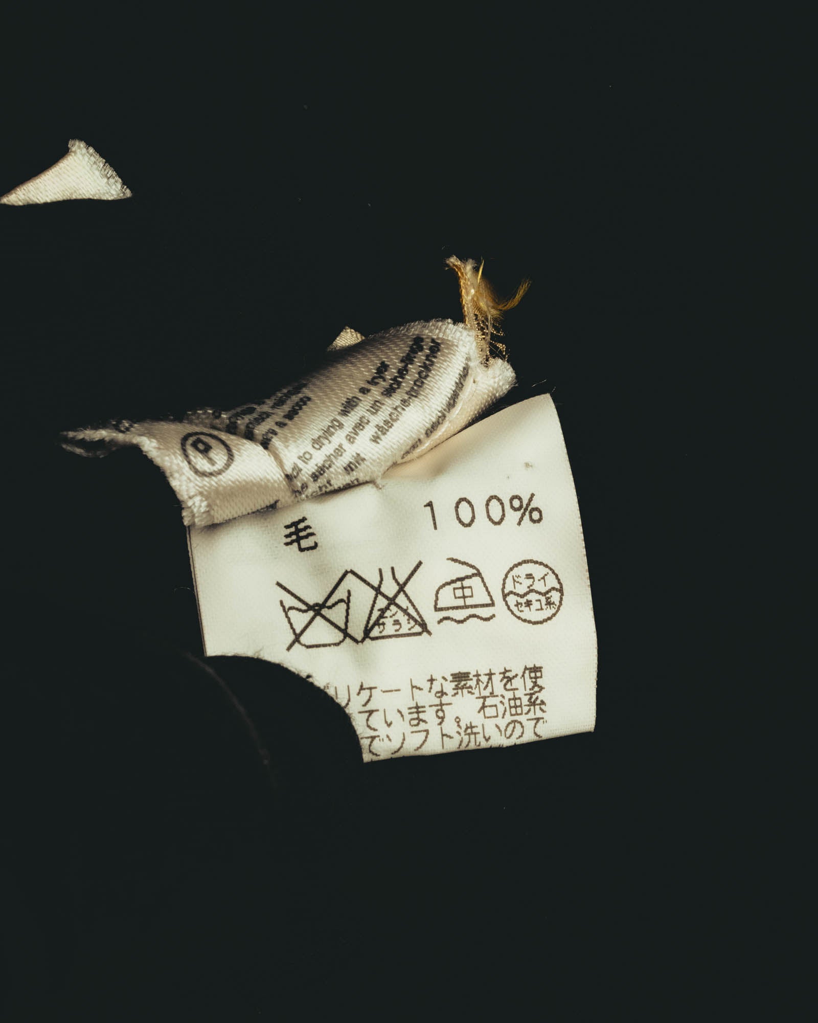 旧JIS系の洗濯表示と「毛 100%」表記を確認できる日本語品質表示タグのカット。内側にはイタリア製表記を含む織りタグが重なっている。