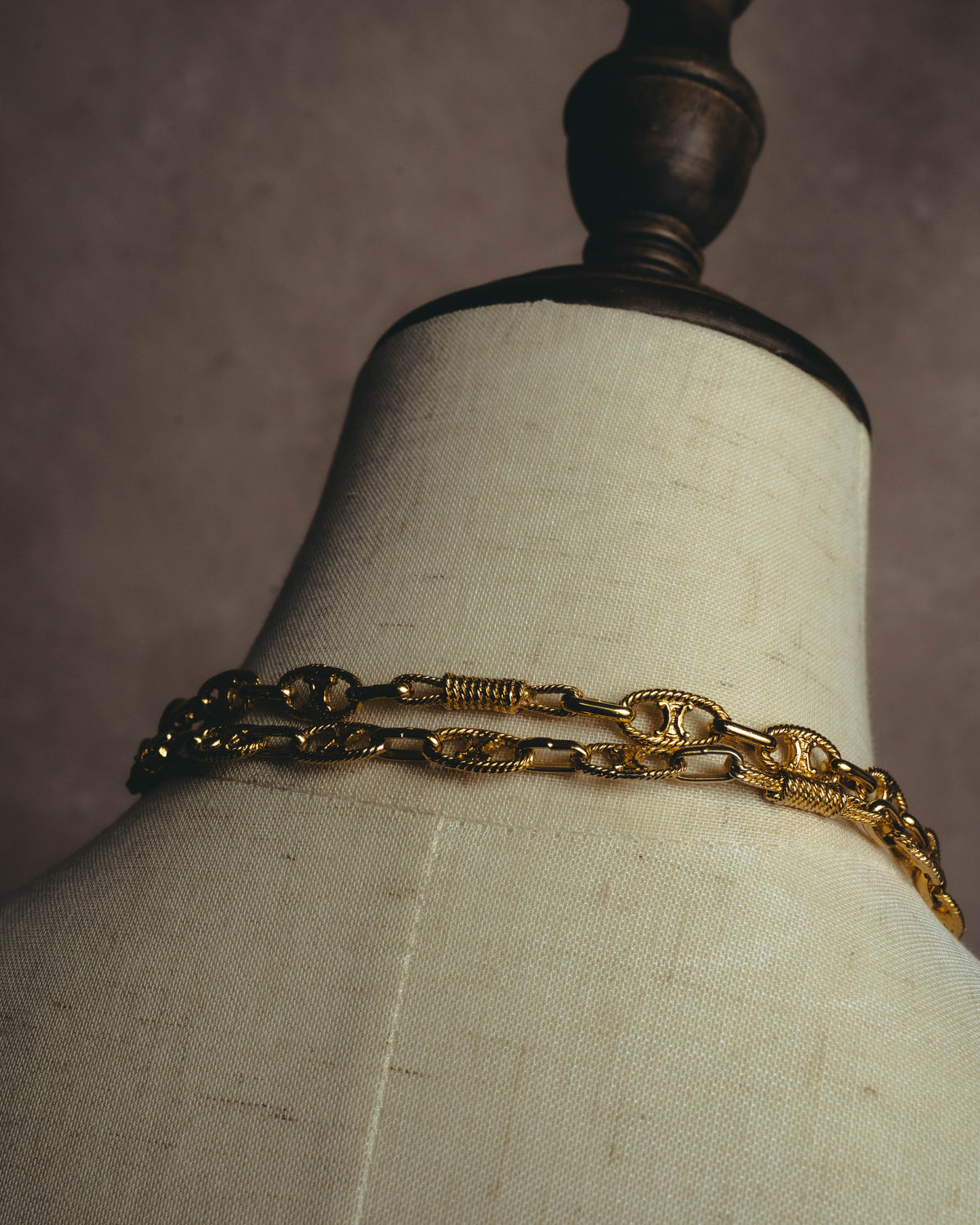 ロープ状の縁取りを施した楕円形モチーフと、中央に横棒を配したリンクが首元に連なるスタイリングカット。巻線状の装飾を加えた細長いパーツを含む、ゴールドトーンのリンク構成が確認できます。
