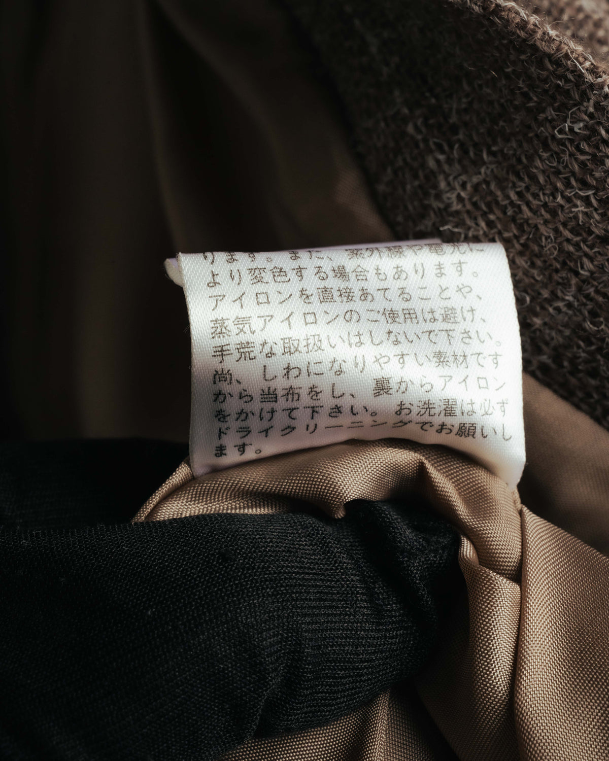 内側に配された日本語主体の品質表示タグを捉えたカット。滑りの良いブラウン系の総裏地と、表地の起毛感を帯びた織り目も確認できます。