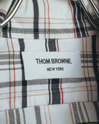 ホワイト、ブラック、グレーに細いレッドラインが交差するタータンチェック地に配された、「THOM BROWNE. NEW YORK」表記のネームタグ。