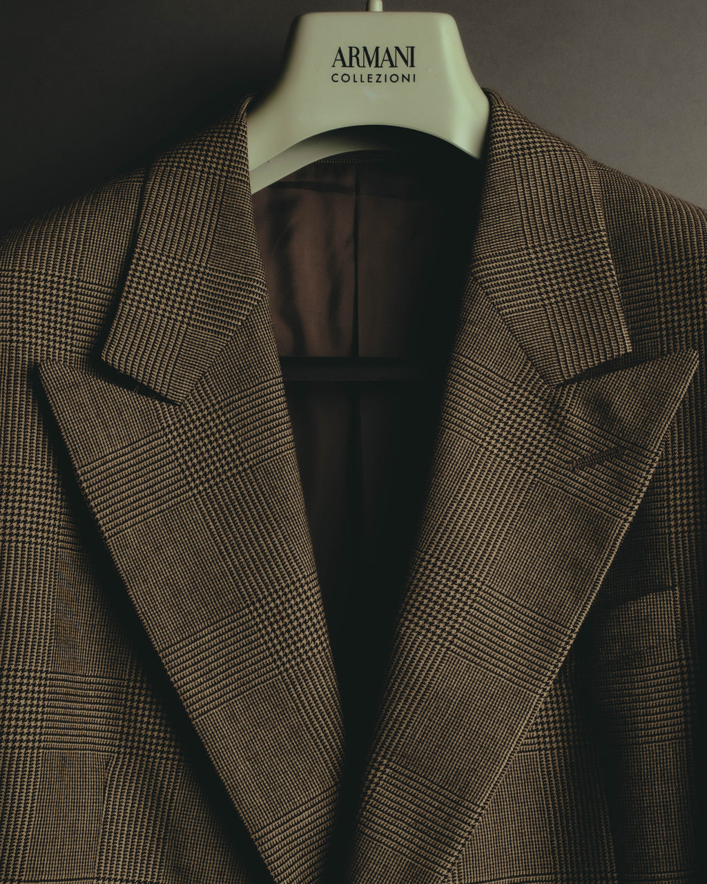ジャケット前身頃の幅広のノッチドラペルを捉えたディテールカット。ブラウンからトープを基調に濃茶のラインで描かれたグレンチェックと、内側の落ち着いたブラウンの裏地が確認できます。