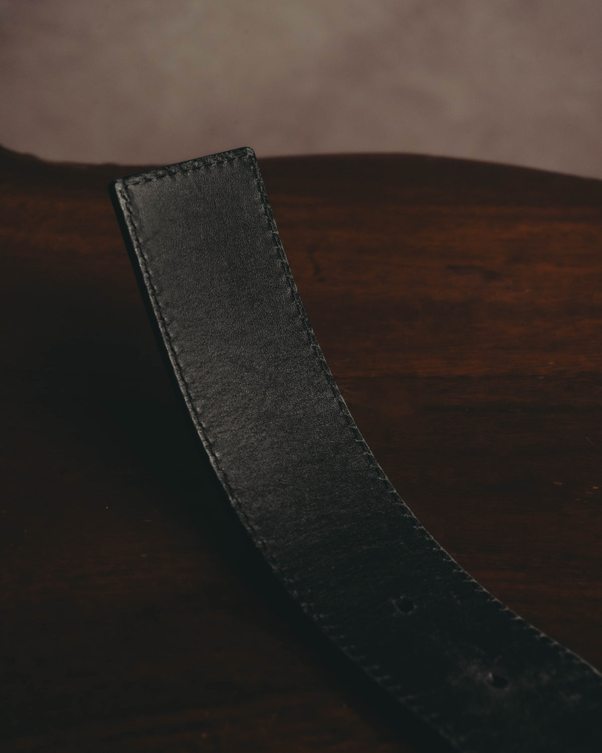 ブラックのベルト本体の剣先から中ほどにかけてを捉えた素材カット。滑らかな表情のレザーと見受けられる質感、両端のステッチ、調整穴が確認できます。