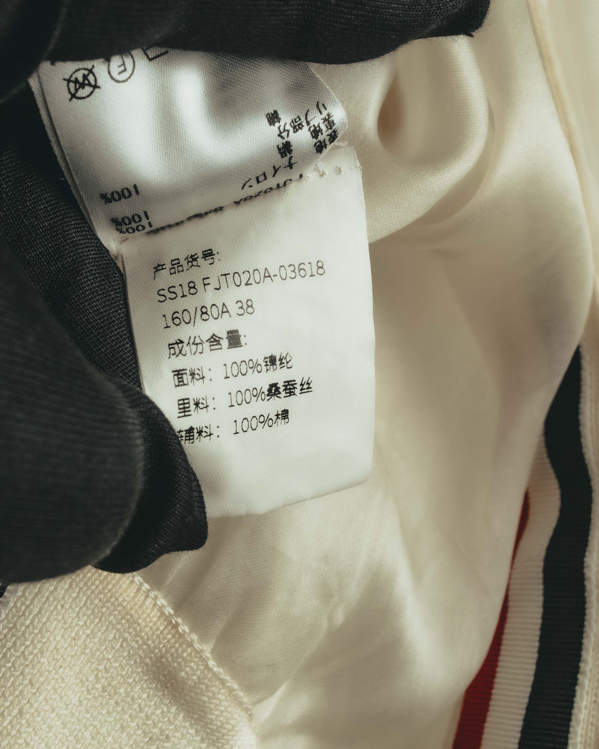 製品コード「SS18FJT020A-03618」とサイズ表記を確認できる品質表示タグのカット。表地ナイロン100%、裏地シルク100%、補料コットン100%の素材表記が写っています。