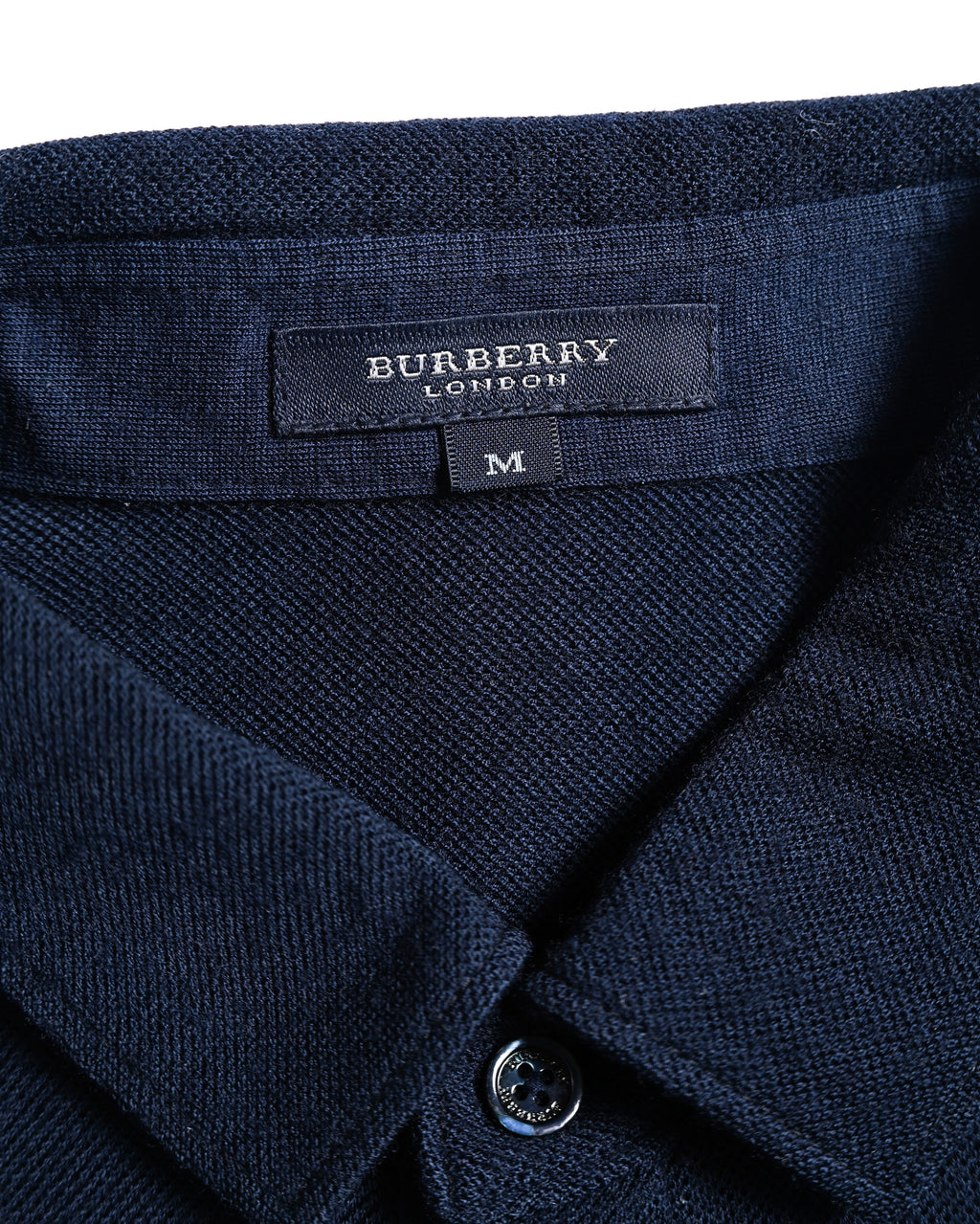 ネイビーのニット襟内側に配されたBURBERRY LONDONタグと、前立てのロゴ刻印入りシェルボタンを捉えたカット。