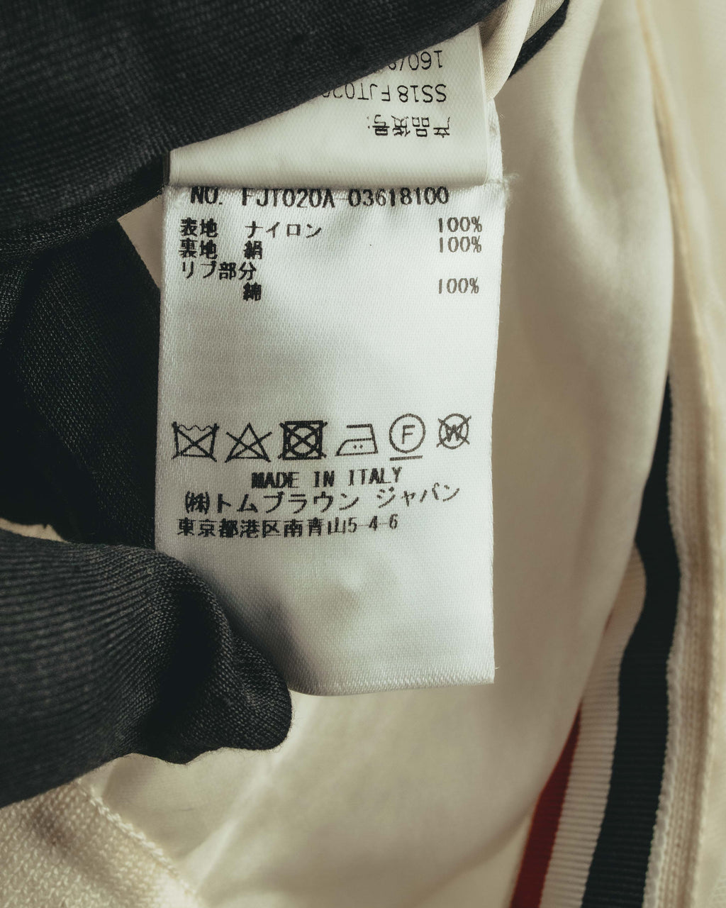 品質表示タグに製品コード「FJT020A 03618100」と、表地ナイロン100％・裏地およびリブ部分シルク100％の素材表記を確認できるカット。