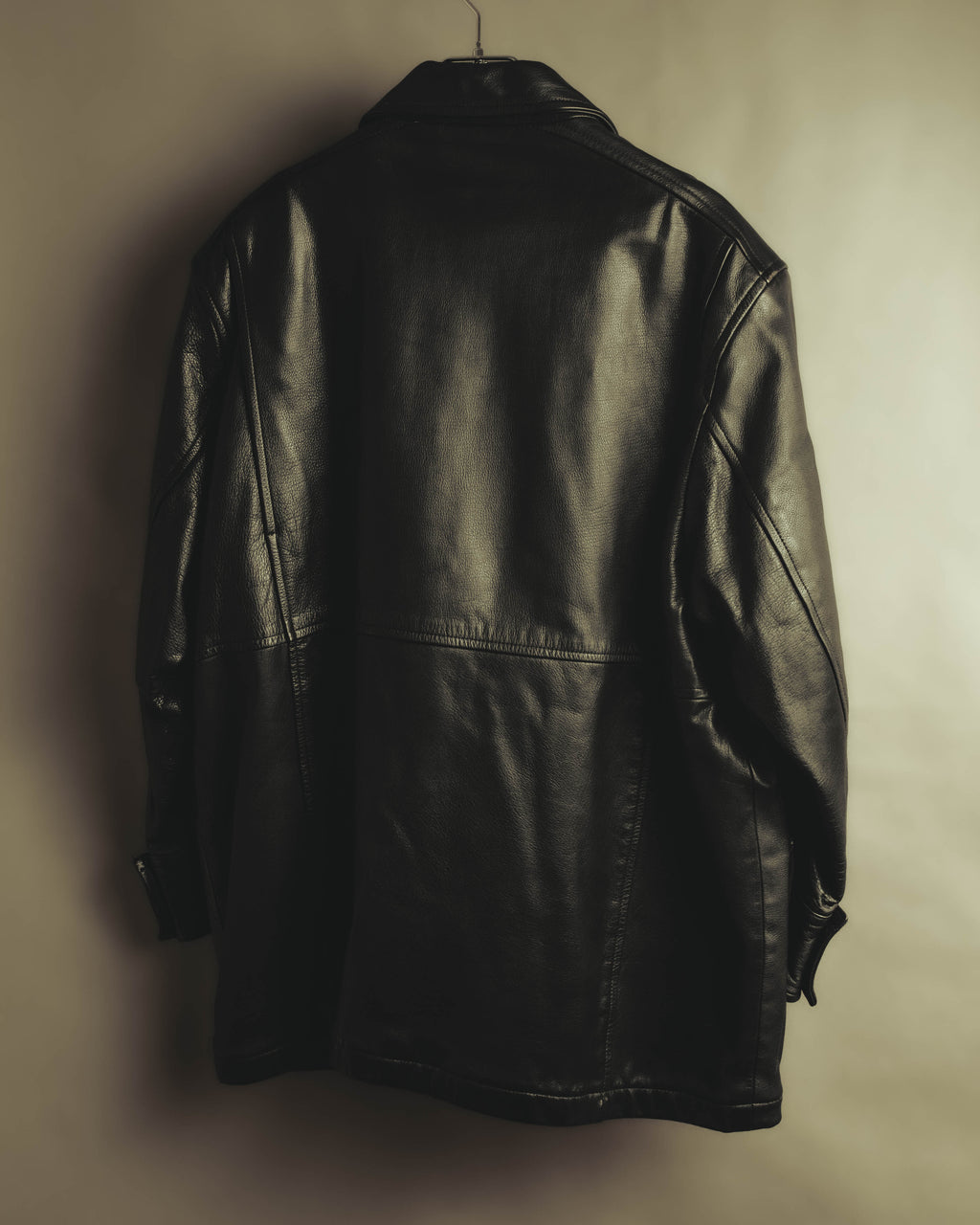 ブラックレザーの背面全体を捉えたカット。肩から身頃へゆとりを持たせたシルエットと、ミドル丈の量感が確認できます。