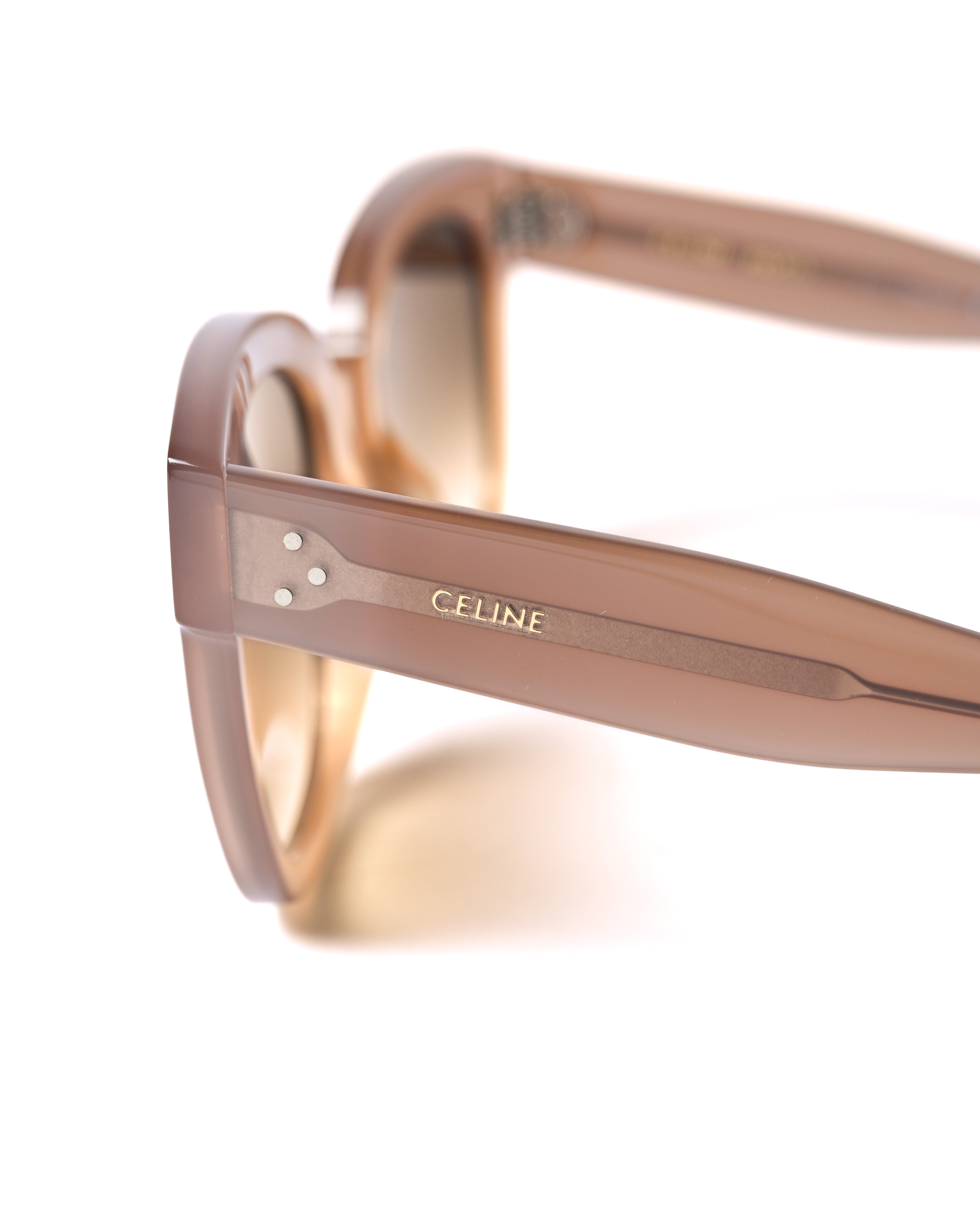 クリアベージュのアセテートテンプルを寄りで捉えたカット。金属芯の上に配されたゴールドの「CELINE」ロゴと、ヒンジ付近の3つのスリードットが確認できます。