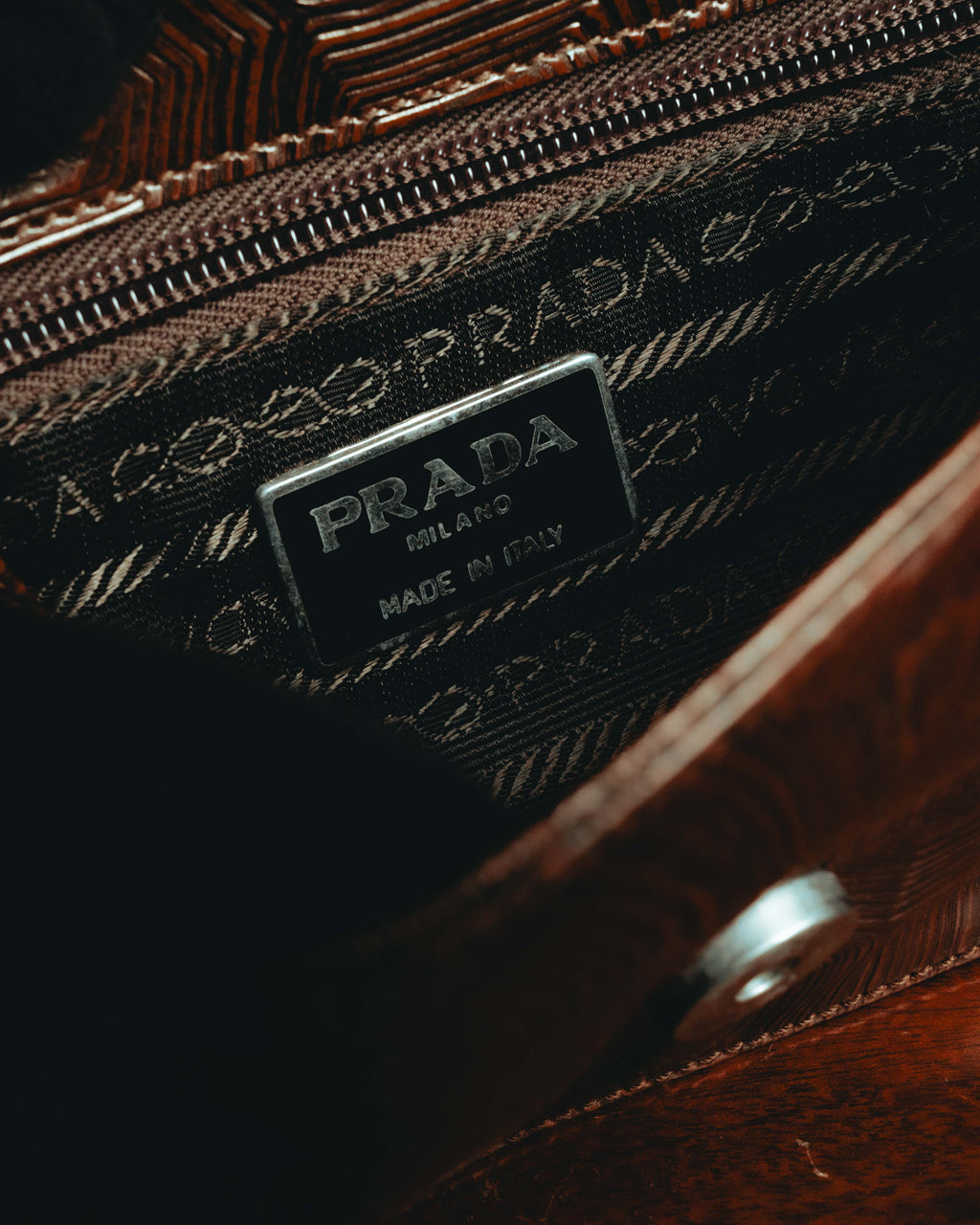 内装に配された「PRADA MILANO MADE IN ITALY」表記の内装プレートと、ロープ状モチーフを反復した織りジャカードのディテール。開口部のジッパーと内装の仕立てを確認できるカット。