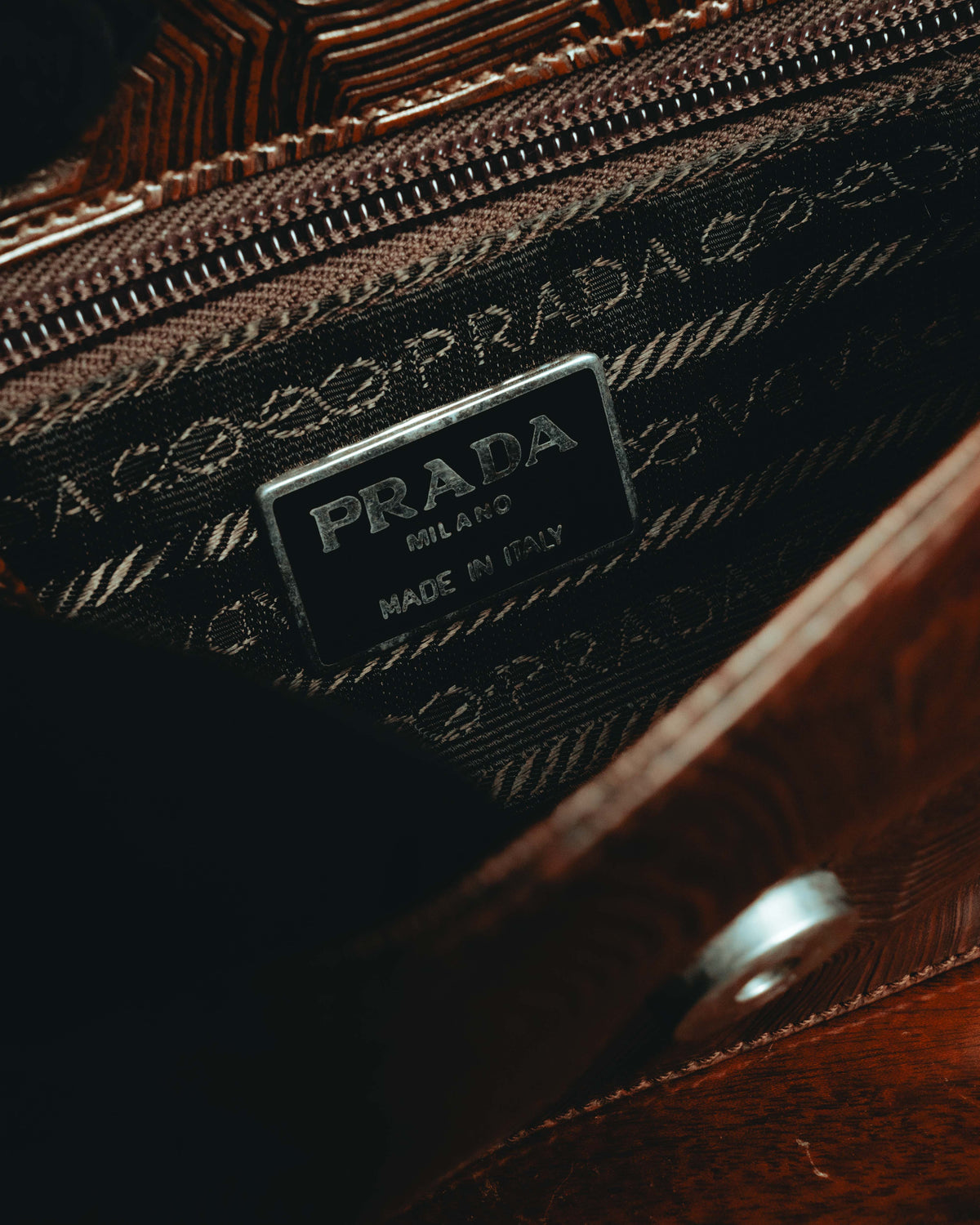 内装に配された「PRADA MILANO MADE IN ITALY」表記の内装プレートと、ロープ状モチーフを反復した織りジャカードのディテール。開口部のジッパーと内装の仕立てを確認できるカット。