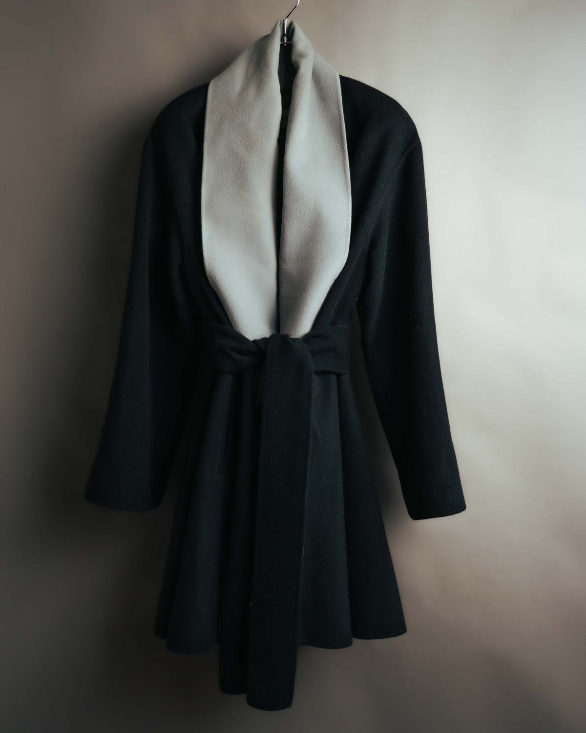ブラックの身頃に淡いグレーのロングショールカラーを配した、フロント全体のカット。共布ベルトでウエストを絞った、裾へ広がるAライン調のシルエットが確認できます。