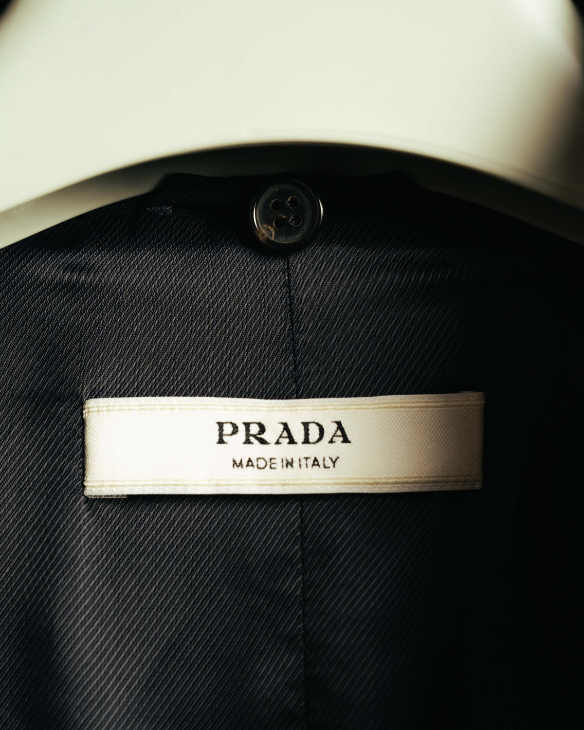 内側に配された生成り色の織りタグ。PRADAロゴとMADE IN ITALY表記が確認でき、上部には黒い4穴ボタンが写る。