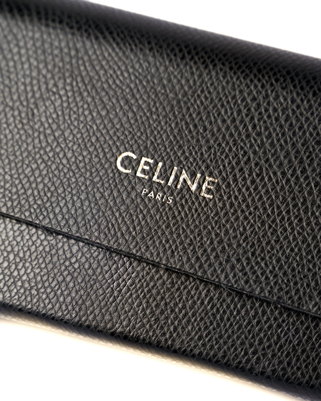 付属するシボ革仕様のブラックレザーケースに配された、CELINE PARISのロゴ刻印を捉えたディテールカット。細かなシボのあるレザー表面とフラップの縁が確認できます。
