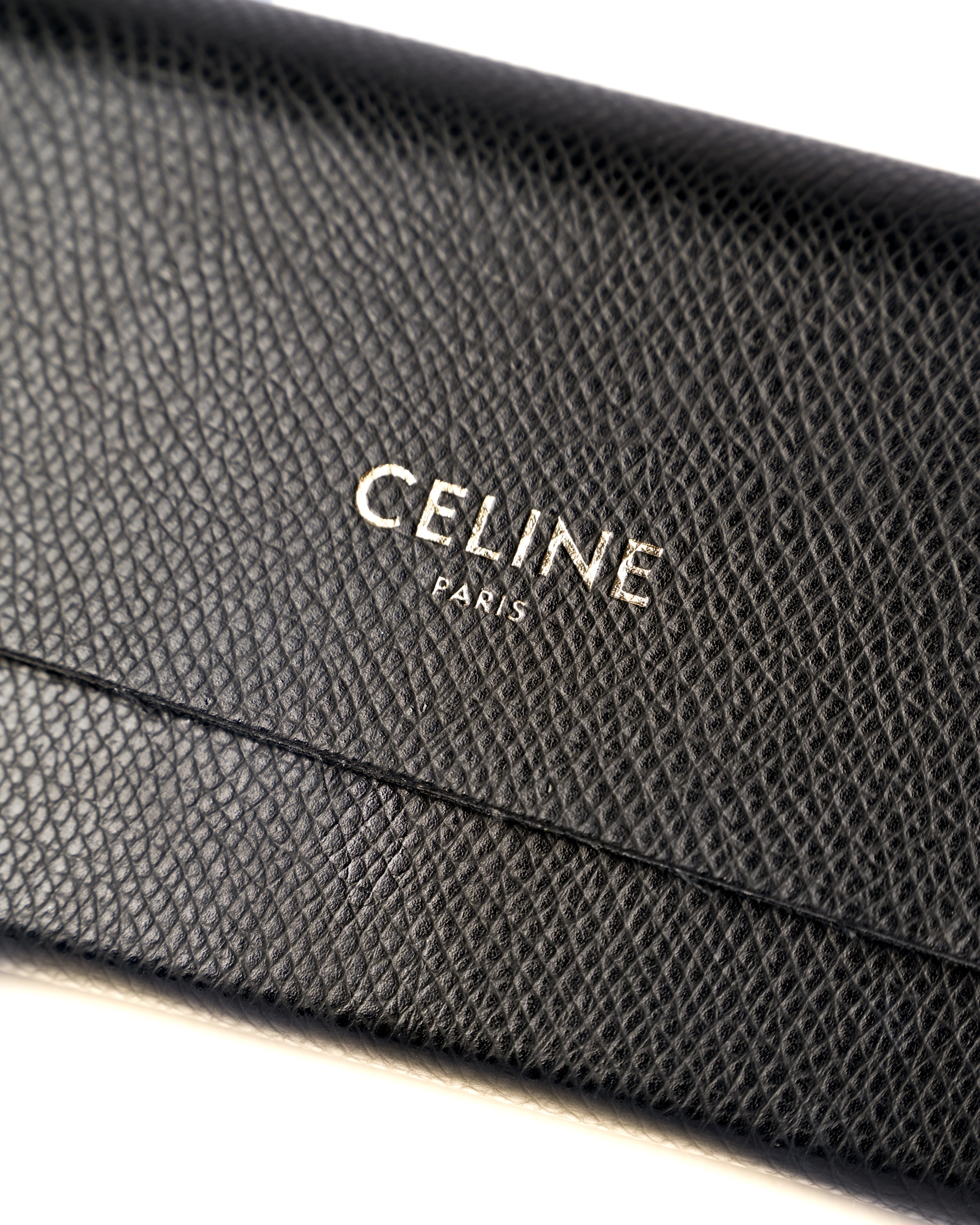付属するシボ革仕様のブラックレザーケースに配された、CELINE PARISのロゴ刻印を捉えたディテールカット。細かなシボのあるレザー表面とフラップの縁が確認できます。