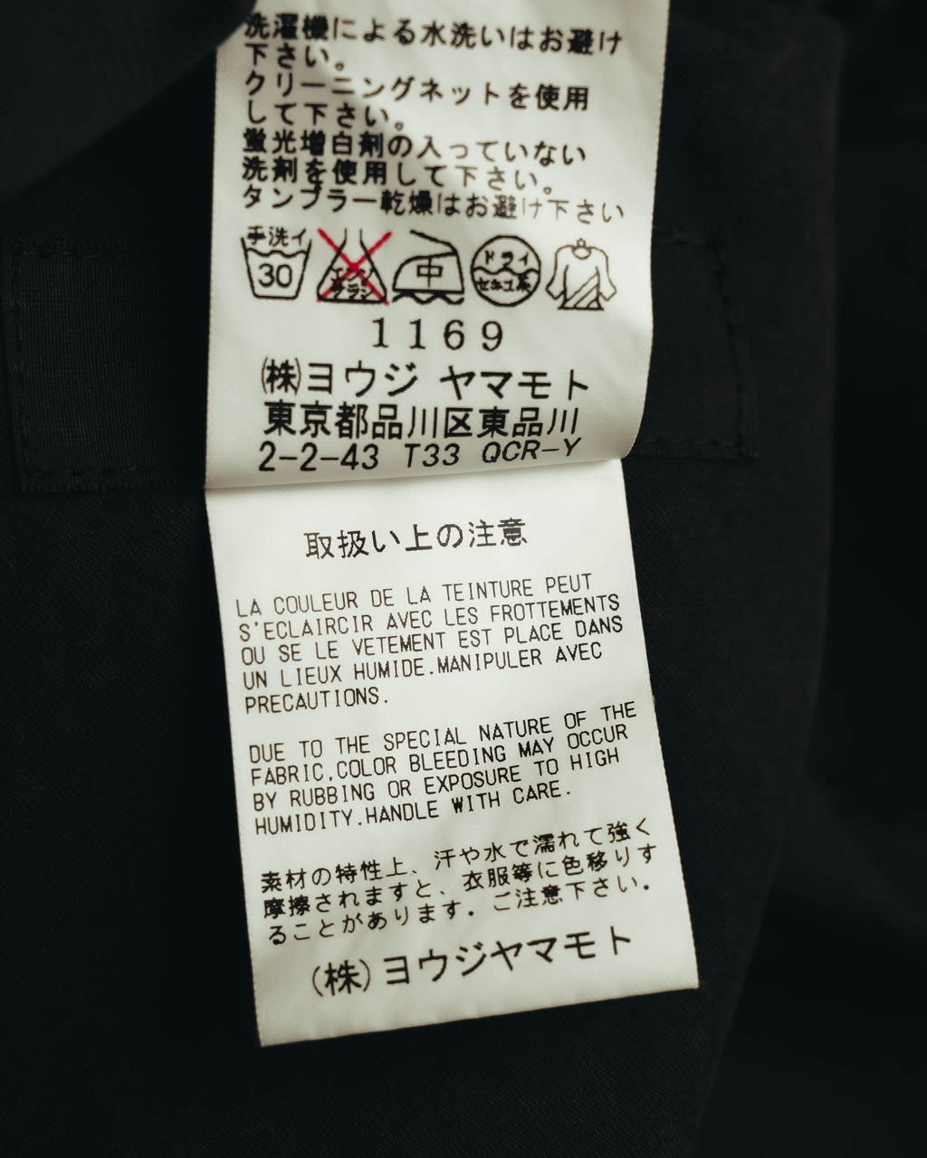 洗濯表示と取扱い上の注意を記した内側のケアタグ。水洗い・タンブラー乾燥に関する注意書きと、ヨウジヤマモトの表記が確認できるカット。
