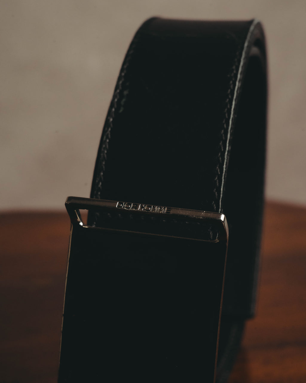 鏡面仕上げのプレートバックル上部に配されたDIOR HOMME刻印を捉えたディテールカット。ブラックのベルト本体と両端のステッチも確認できます。