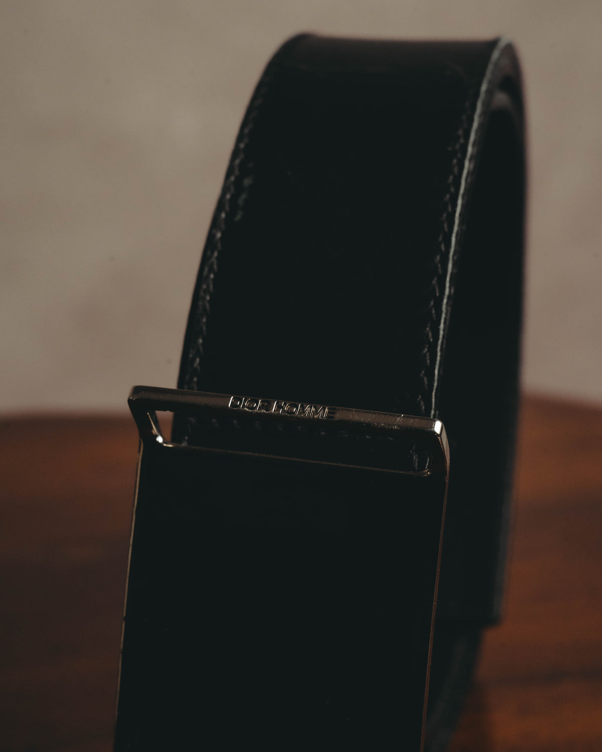 鏡面仕上げのプレートバックル上部に配されたDIOR HOMME刻印を捉えたディテールカット。ブラックのベルト本体と両端のステッチも確認できます。