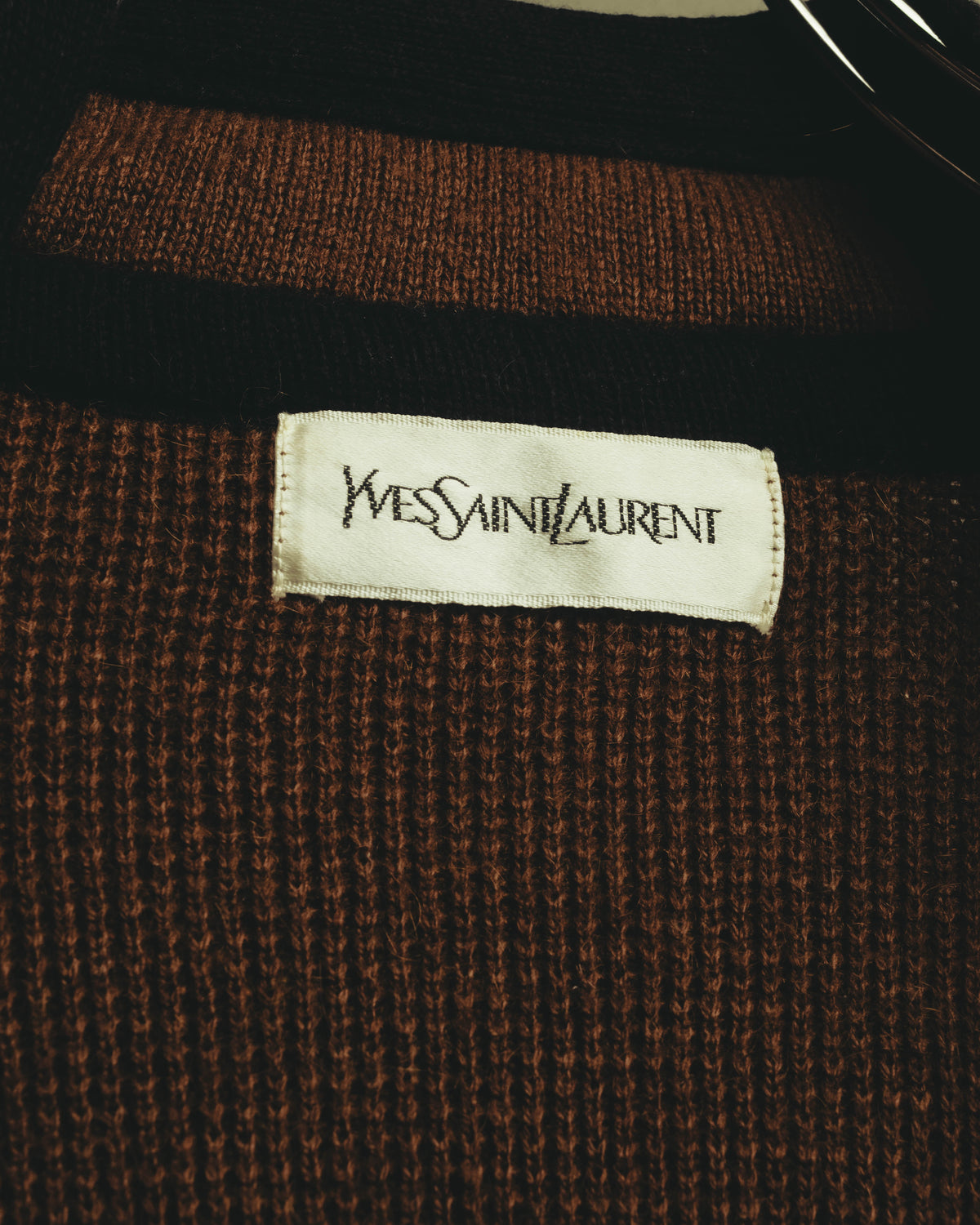 ブラウンの起毛感のあるニット生地に縫い付けられた、Yves Saint Laurentのブランドタグを確認できるカット。