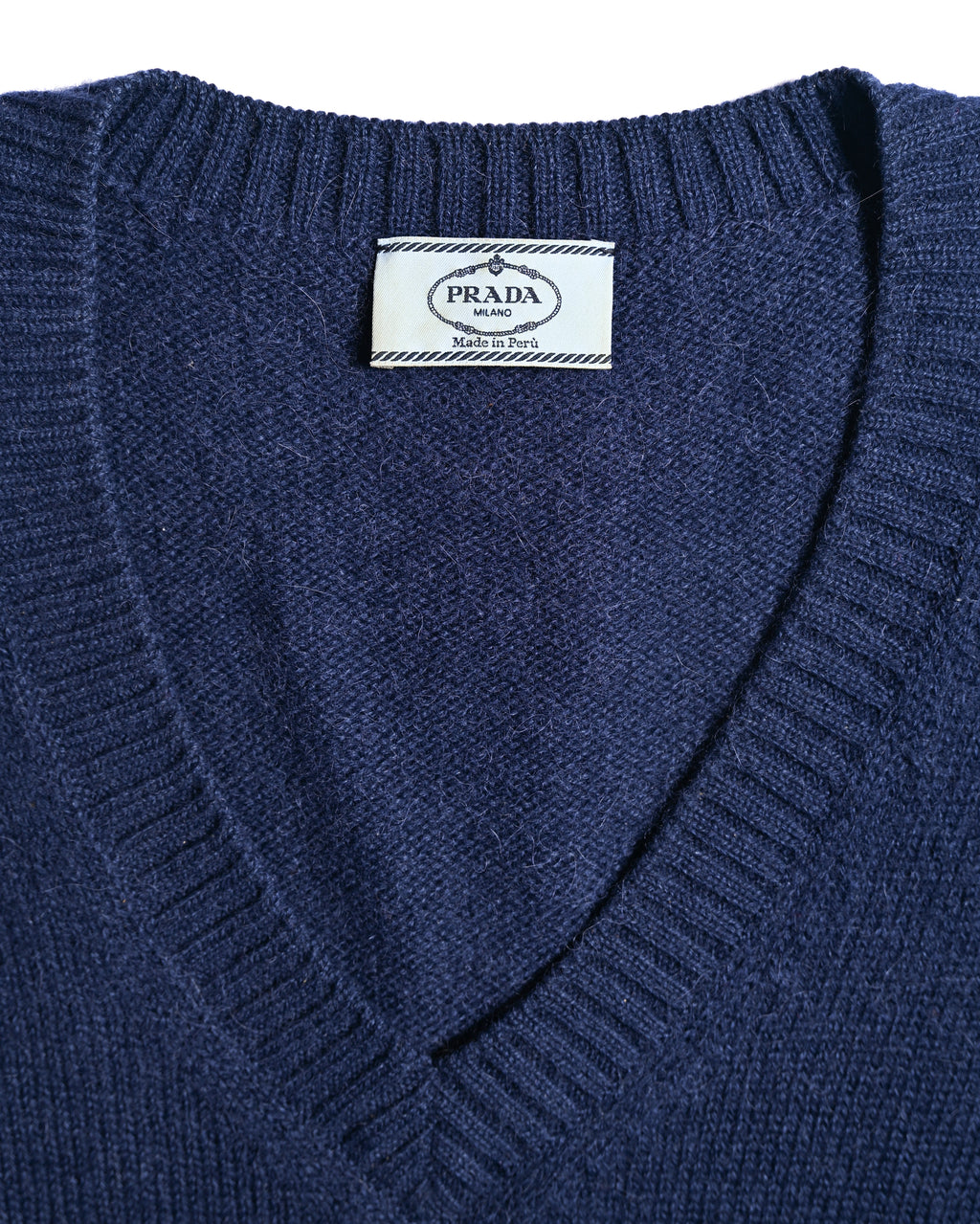 PRADA MILANOおよび「Made in Peru」表記が読める首元の内タグ。深く切り込まれたVネックラインと、衿ぐりのリブ編みも確認できるカット。