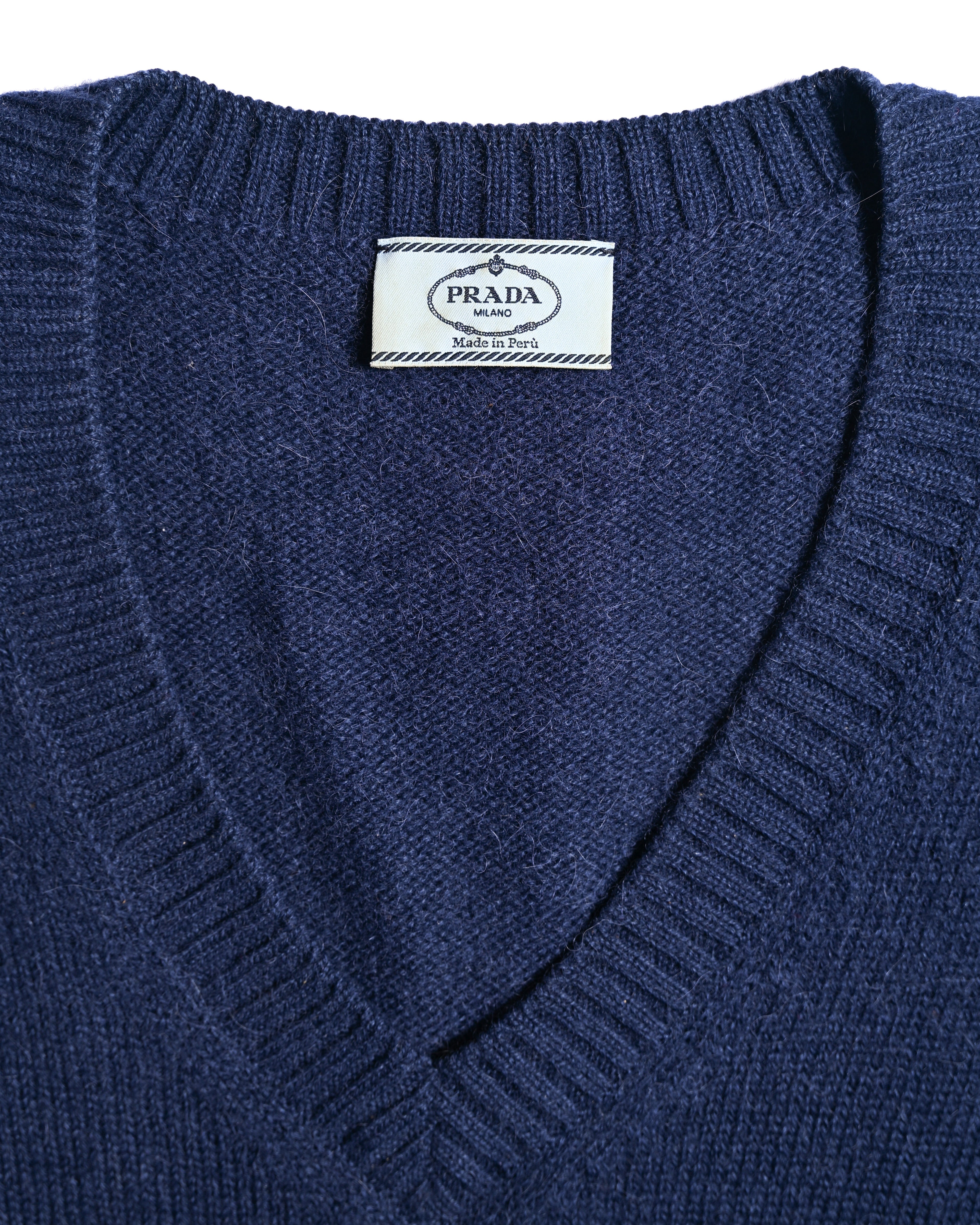 PRADA MILANOおよび「Made in Peru」表記が読める首元の内タグ。深く切り込まれたVネックラインと、衿ぐりのリブ編みも確認できるカット。