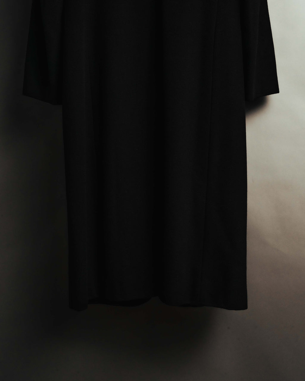 ブラックのウールカシミヤ混紡生地が裾へまっすぐ落ちる、ロングコート下部のディテールカット。足元近くまで伸びる着丈と、縦のラインを強調するストレートなシルエットが確認できます。