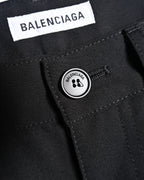 フロントのブランド名刻印入りオリジナルトップボタンと、ウエスト内側に配した「BALENCIAGA」ホワイトタグを捉えたディテールカット。ブラックのウールギャバジン調生地とウエスト周りの縫製も確認できます。