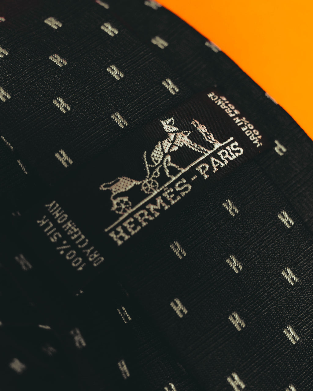 剣先に織りで表現された馬車図案とHERMES PARISのシグネチャーを捉えたディテールカット。周囲には銀白色に見える糸によるHモチーフの反復が確認できます。