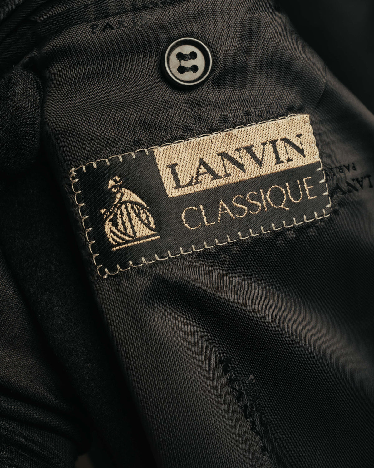母娘図像を伴うLANVIN CLASSIQUEの織りネームを捉えた内側のタグカット。ロゴを反復したジャカード裏地と、内側に配されたボタンも確認できます。