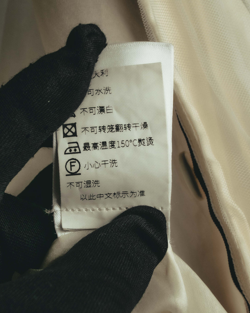 内側に配された洗濯表示タグのクローズアップ。オフホワイトのチュール素材と滑らかな裏地を背景に、ケア表記を確認できるカット。