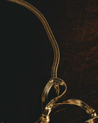 細やかな編み目を持つゴールドカラーの扁平チェーンと、フロント中央で重なる立体的なリボン構造を捉えたディテールカット。