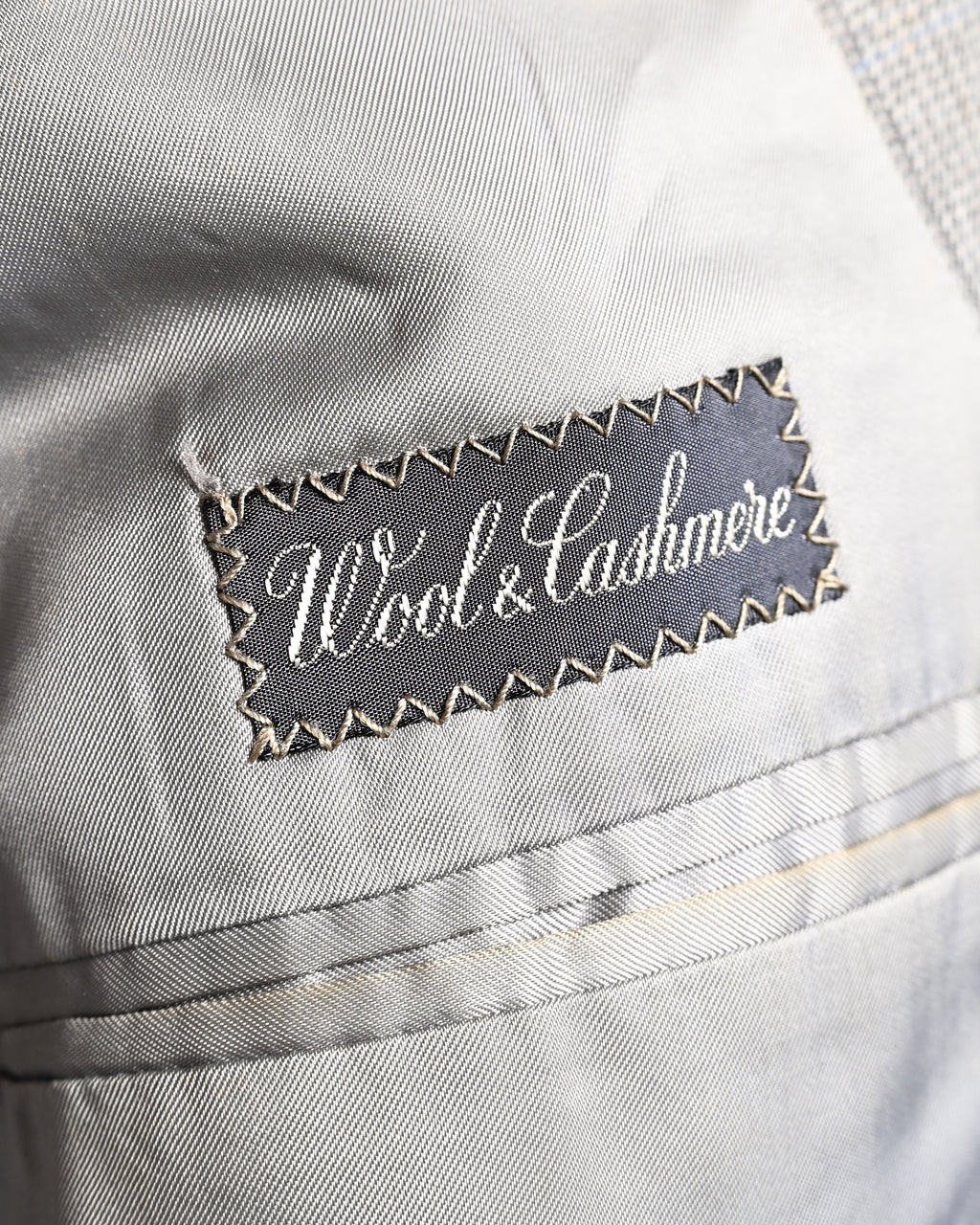 滑らかなグレー系の総裏地に配された「Wool & Cashmere」表記の服地ネーム。内ポケットまわりの袋布とパイピングの仕様も確認できる内側のカット。