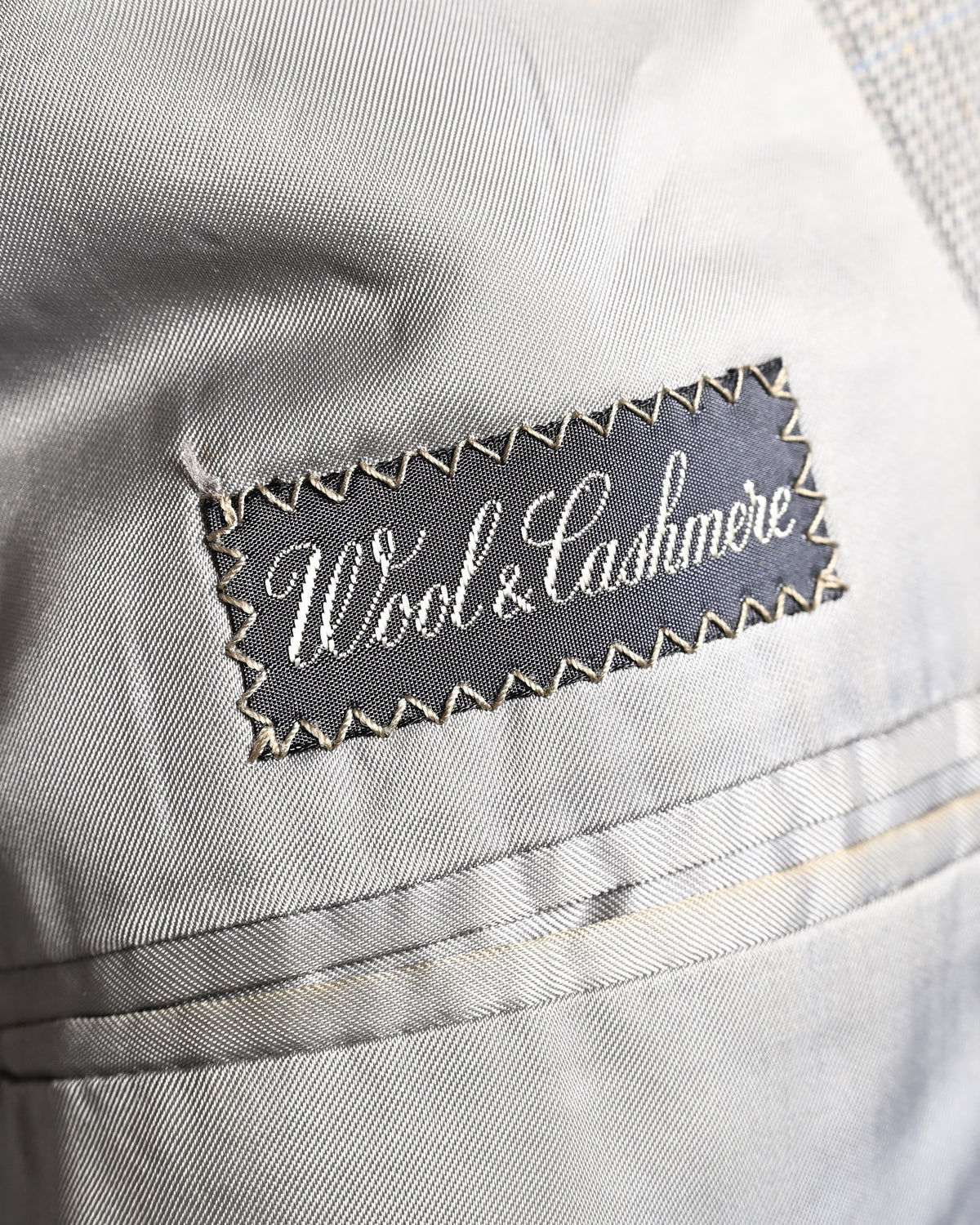 滑らかなグレー系の総裏地に配された「Wool & Cashmere」表記の服地ネーム。内ポケットまわりの袋布とパイピングの仕様も確認できる内側のカット。