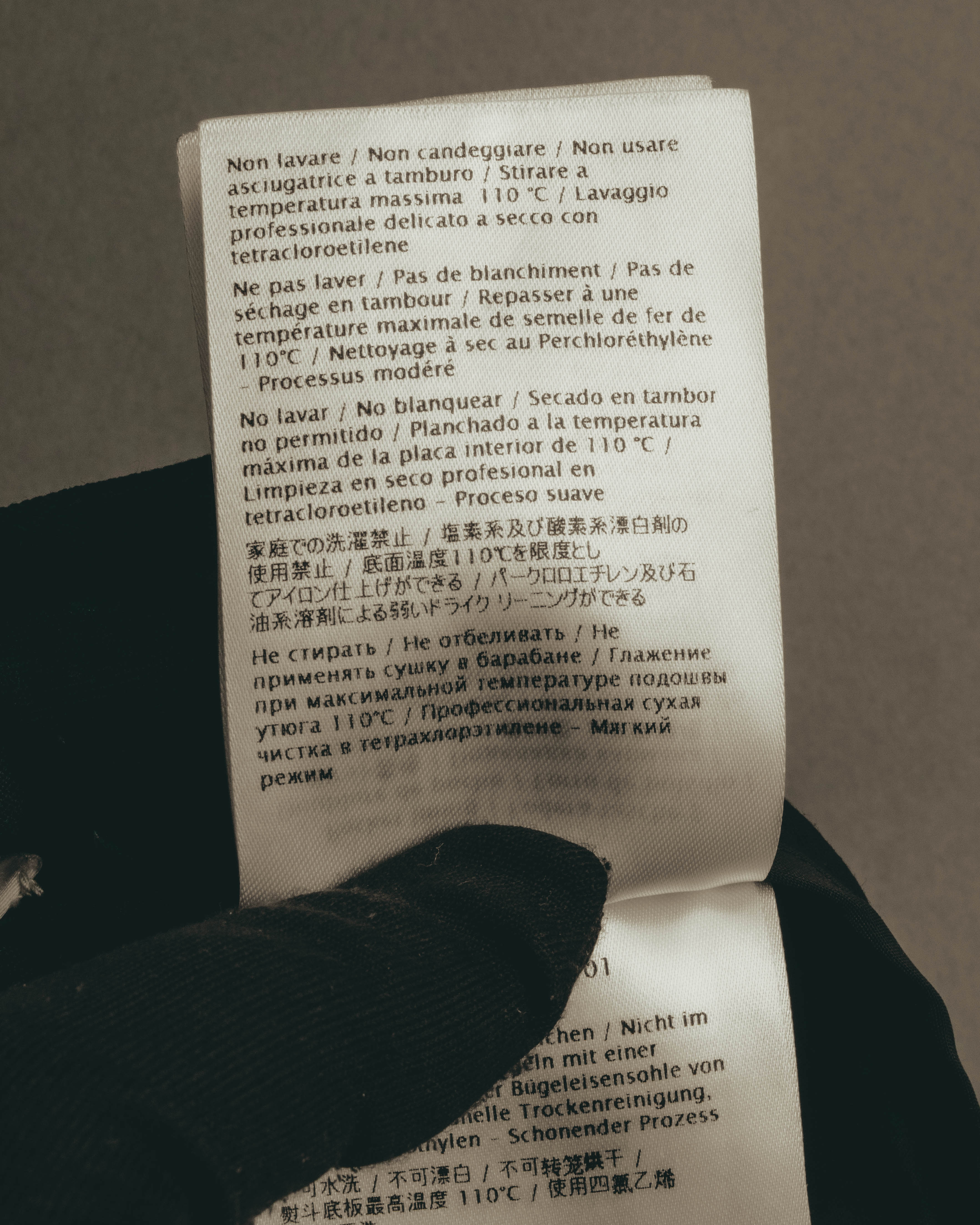 多言語でケア方法が記載された内側の洗濯表示タグ。家庭での洗濯不可、110℃を上限とするアイロン仕上げ、テトラクロロエチレンによる弱いドライクリーニングの表記を確認できるカット。