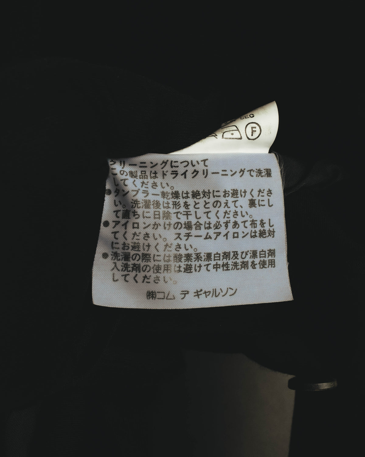 内側に配された洗濯表示タグのクローズアップ。ドライクリーニング表示と裏地素材のキュプラ表記を確認できるカットです。