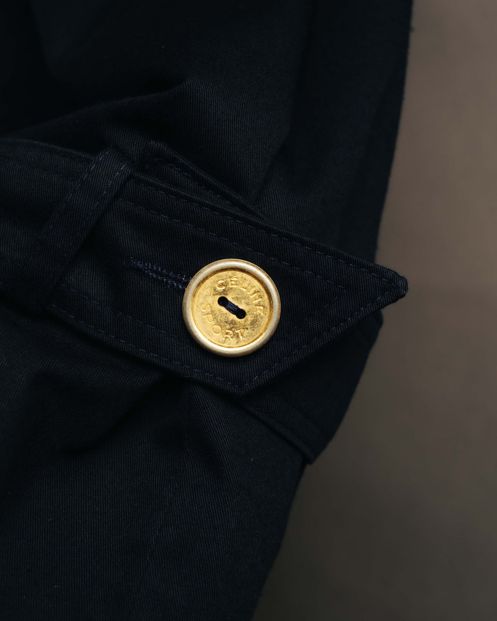 ダークネイビーの袖口ストラップに配された、CÉLINE SPORT刻印入りゴールドボタンのディテールカット。綾織り調のコート生地とステッチも確認できます。