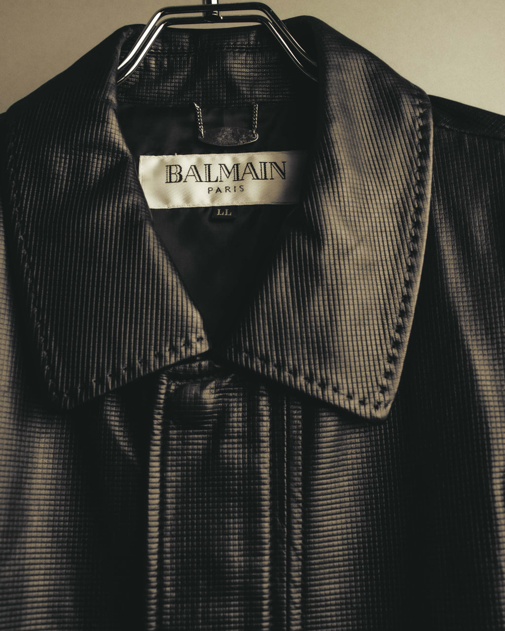 襟元内側に配された「BALMAIN PARIS」表記のブランドタグと、LLサイズ表記を確認できるカット。周囲には細かな格子状の型押しを施したブラックレザーと、襟端のステッチが写っています。