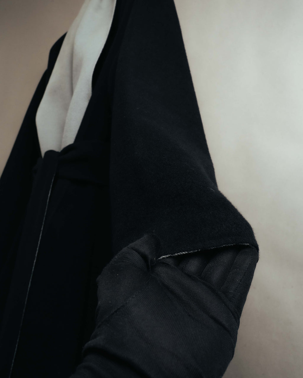 ブラックの起毛感ある身頃に、淡いグレーのロングショールカラーが重なるディテールカット。直線的な袖先と、ウエストで結んだ共布ベルトを確認できます。