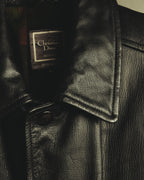 襟元に配された Christian Dior Monsieur Sportswear の織りネームとLサイズ表記を捉えたディテールカット。粒状のシボを持つブラックレザー、大ぶりな襟、フロントの4穴ボタンも確認できます。