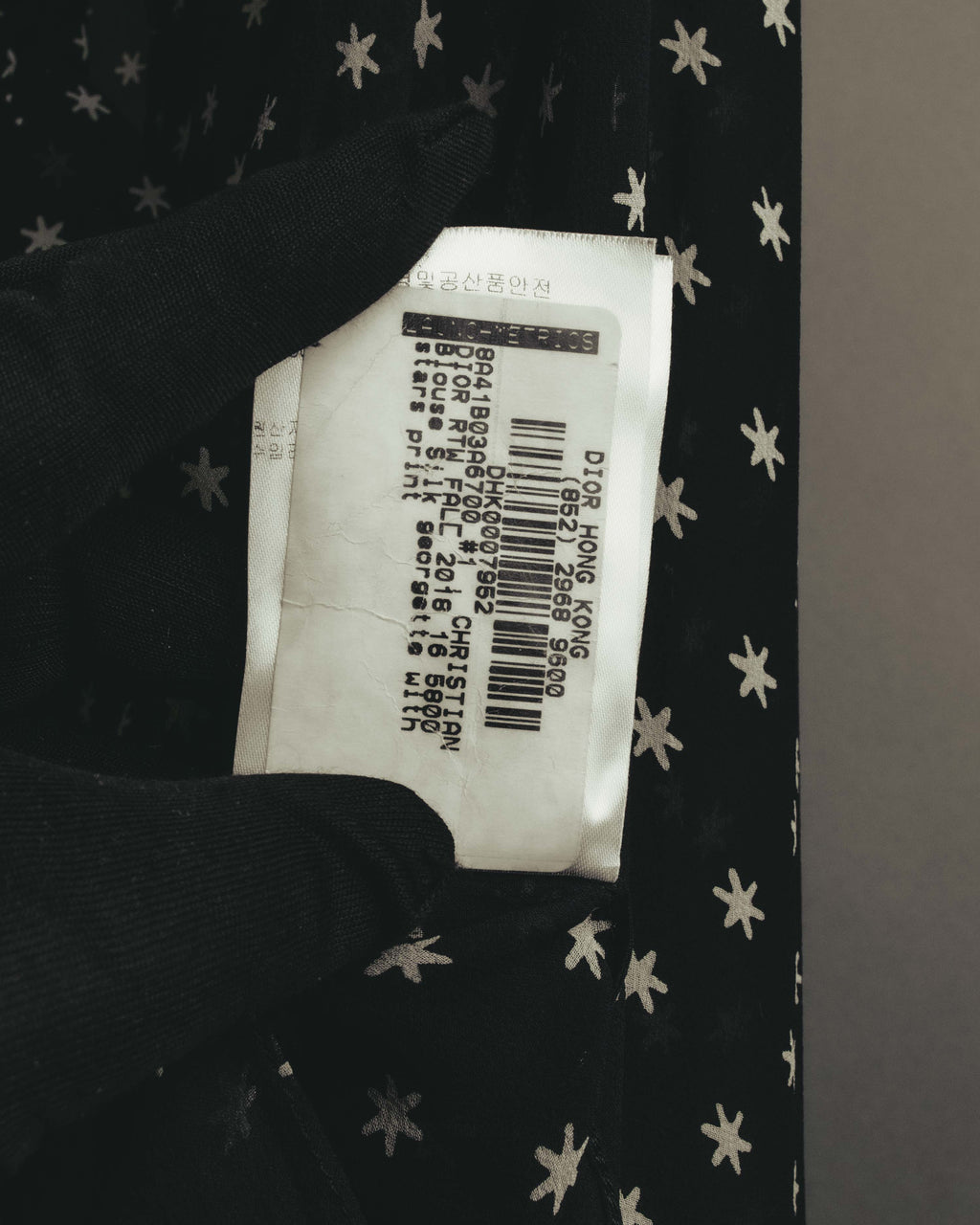 バーコード、品番および「RTW FALL 2018」「PRESS SAMPLE - NOT FOR SALE」の表記が確認できる流通ラベルのカット。ブラック地にアイボリーからグレー系のスターモチーフが写る。
