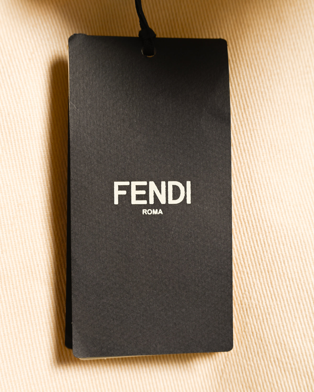 ライトブラウンのコットンドリル生地に添えられた、FENDI ROMAロゴ入りの黒い下げ札。