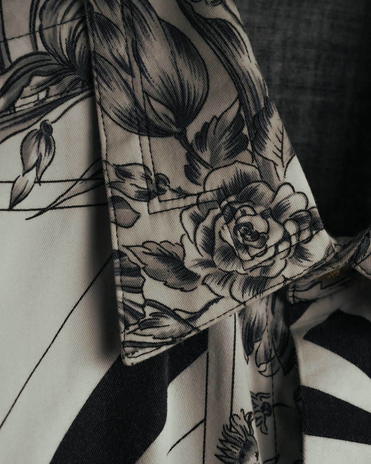 柔らかな曲線を描く線描の花柄を配したカフスのディテール。アイボリー寄りの白地にブラックとグレーで表現された花柄と、端正な縫製が確認できるカット。