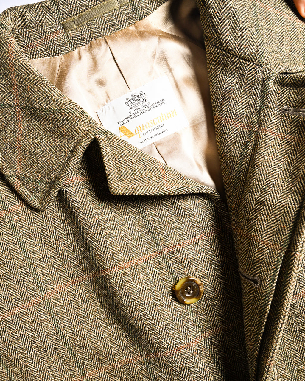 王室御用達を示す表記、Aquascutum OF LONDON、MADE IN ENGLANDの文字を織り込んだ旧仕様のブランドタグを捉えた内側のカット。滑らかな総裏地と、細い格子柄を重ねたヘリンボーン生地、ステンカラーも確認できます。