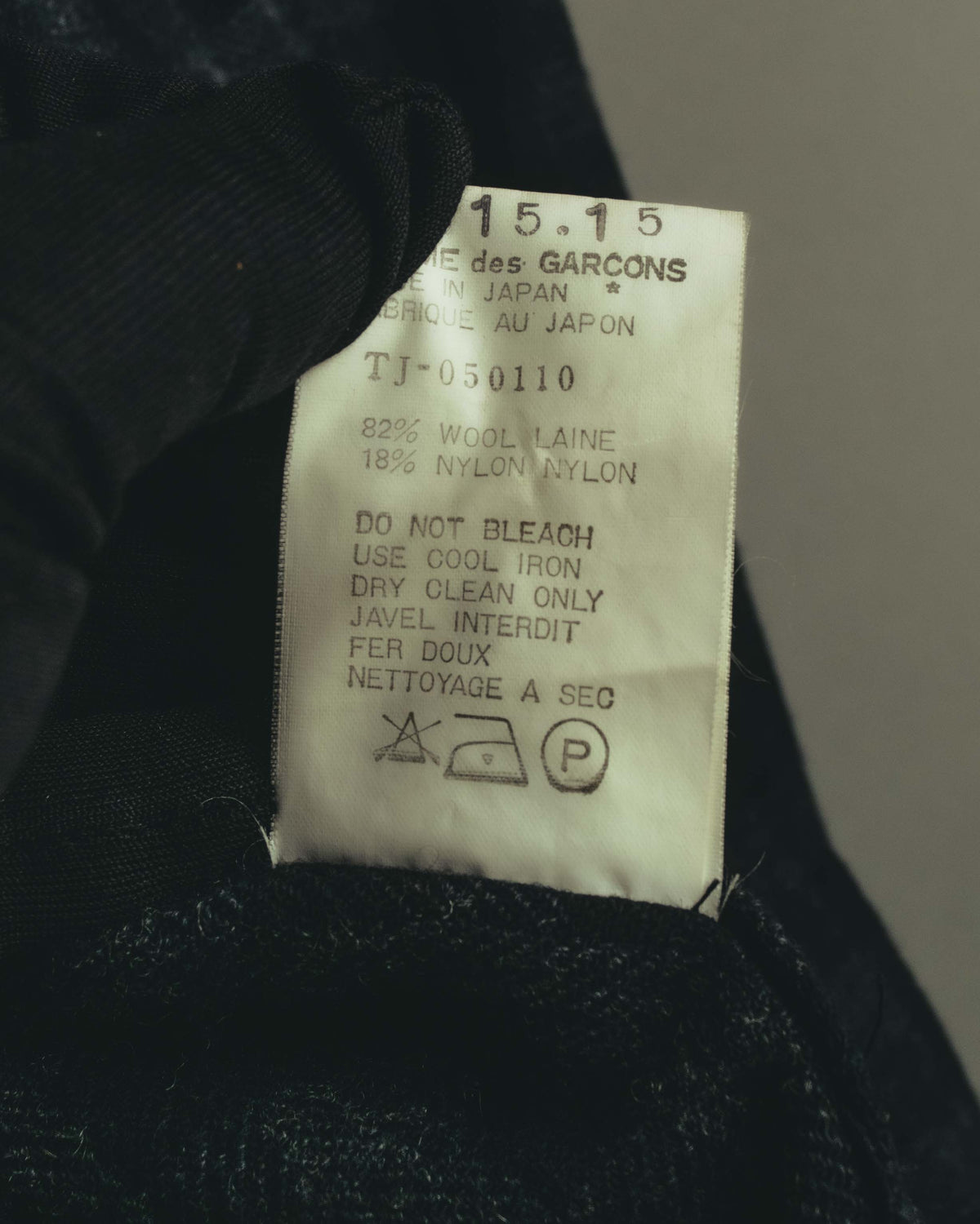 内側に配された品質表示タグのクローズアップ。品番「TJ-050110」、ウール82%・ナイロン18%の混率、ドライクリーニング表記が確認できます。