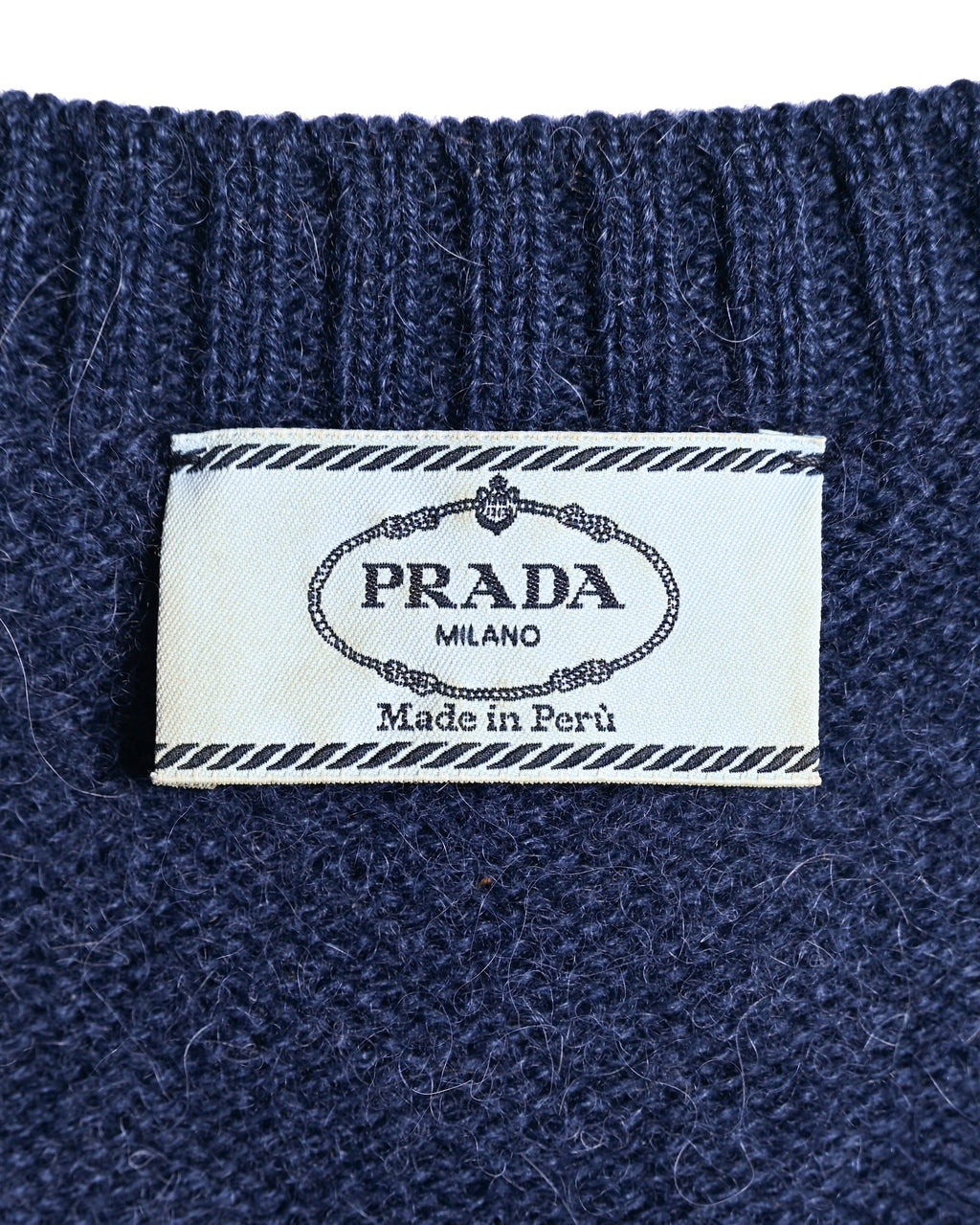ネイビーの起毛感あるニット地に縫い付けられた内タグ。PRADA MILANOおよび「Made in Peru」の表記を確認できるカット。