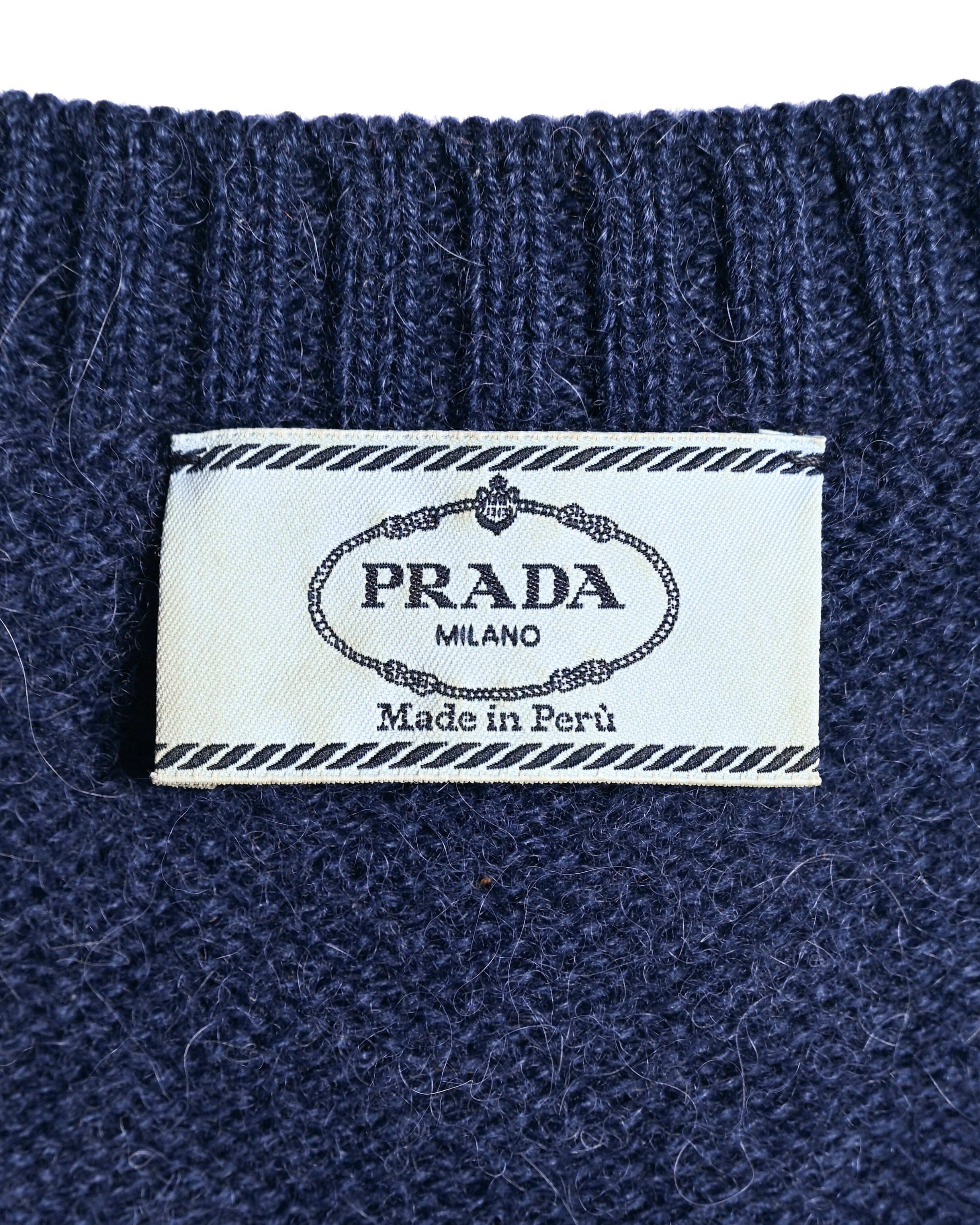 ネイビーの起毛感あるニット地に縫い付けられた内タグ。PRADA MILANOおよび「Made in Peru」の表記を確認できるカット。