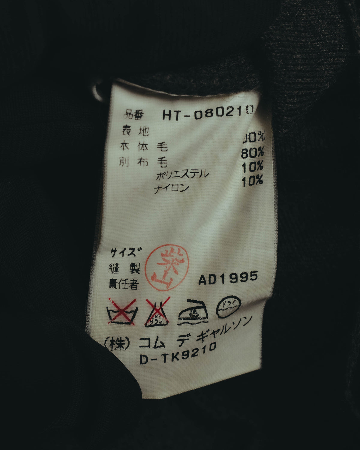 内側の品質表示タグに、AD1995、D-TK9210、株式会社コム デ ギャルソンおよび素材混率の記載が確認できるカット。