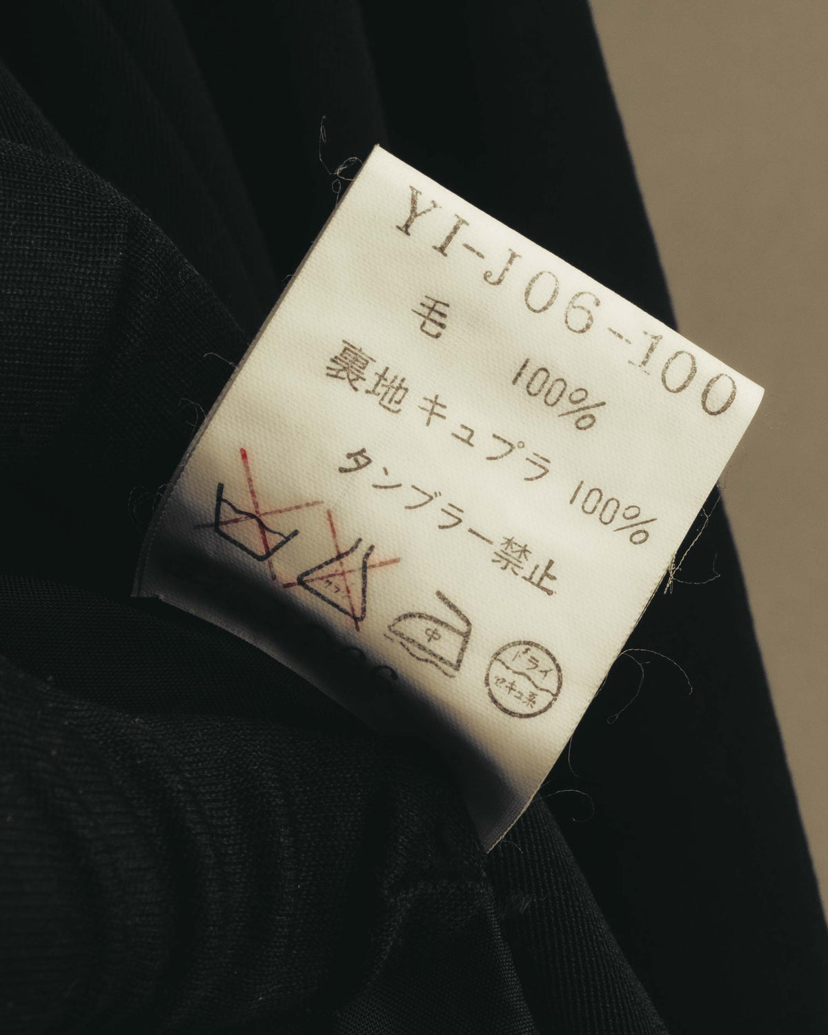 品番「YI-J06-100」と、表地ウール100％・裏地キュプラ100％の素材表記、旧式のJIS洗濯表示が確認できる内タグ。