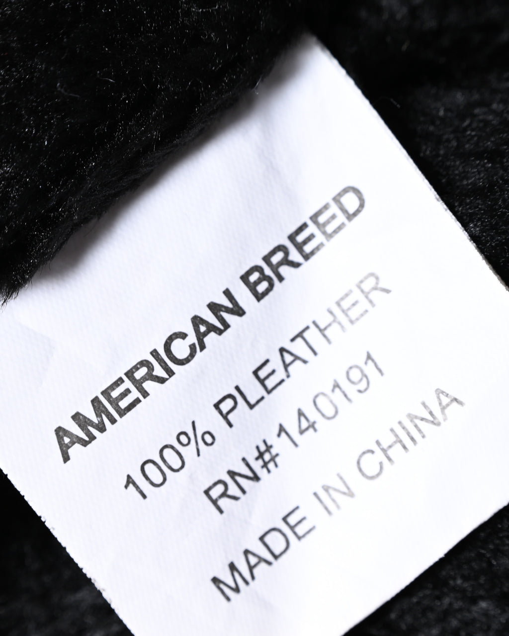 ブラックの起毛ライニングに配された品質表示タグのクローズアップ。AMERICAN BREED表記と、表地100% PLEATHERの素材表記を確認できるカット。