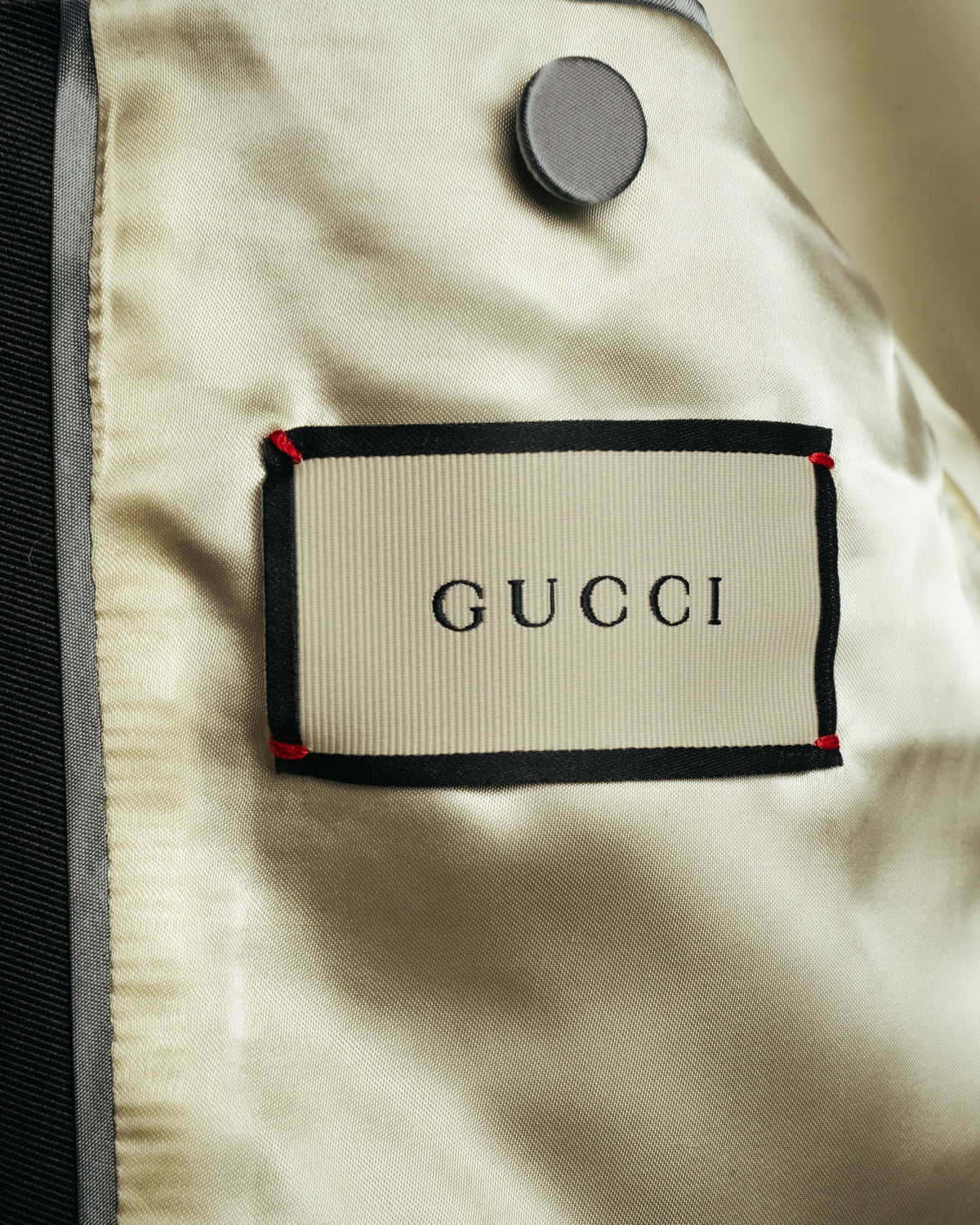 黄みを含んだアイボリーからシャンパンを思わせる総裏地に配されたGUCCIのブランドタグ。上部には内ポケットのボタンが写る内側のディテールカット。
