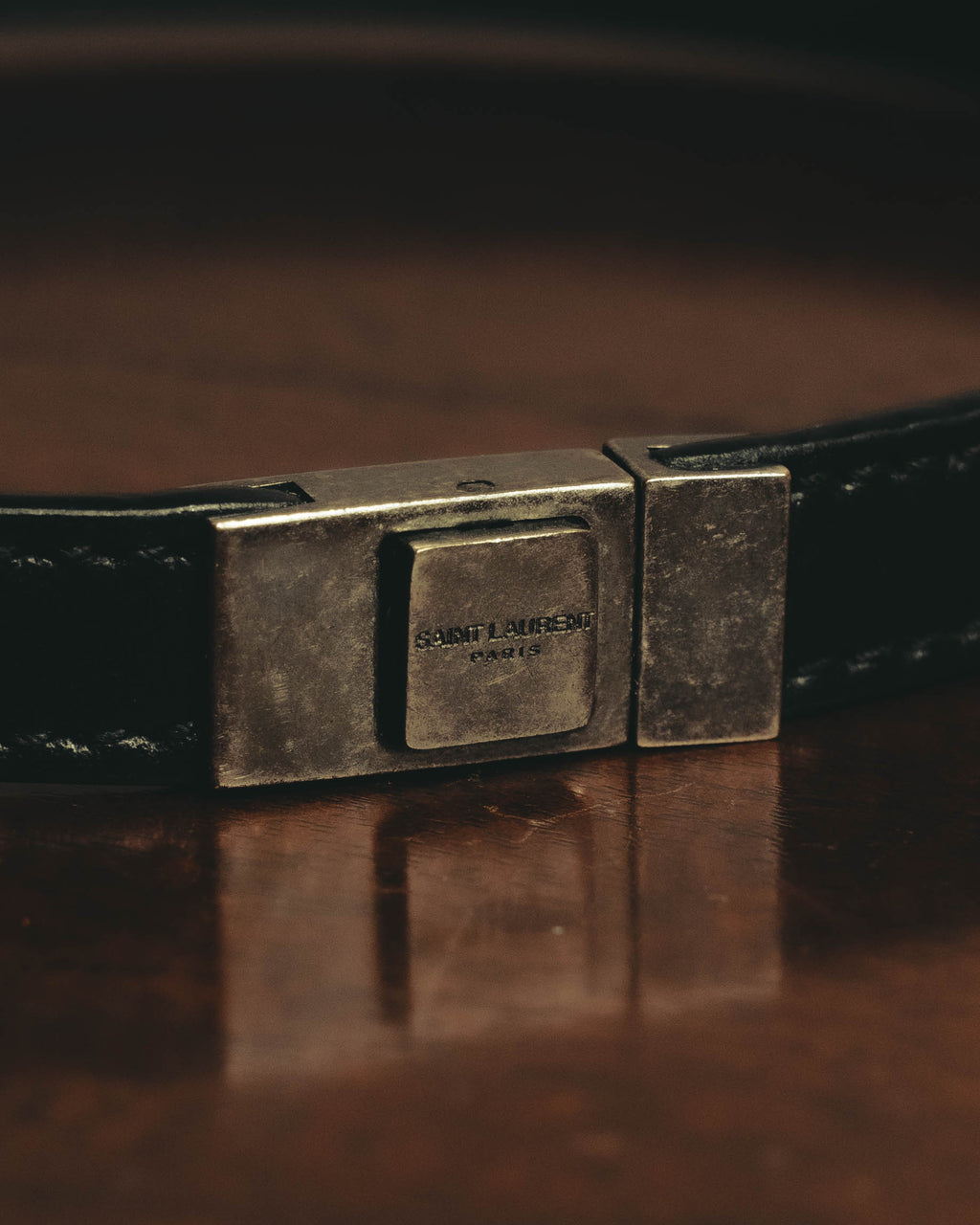 SAINT LAURENT PARISのロゴが刻まれた、スクエア型メタルパーツの留め具（クラスプ）を捉えたディテールカット。直線的なフォルムとヴィンテージライクな金具の表情が確認できます。