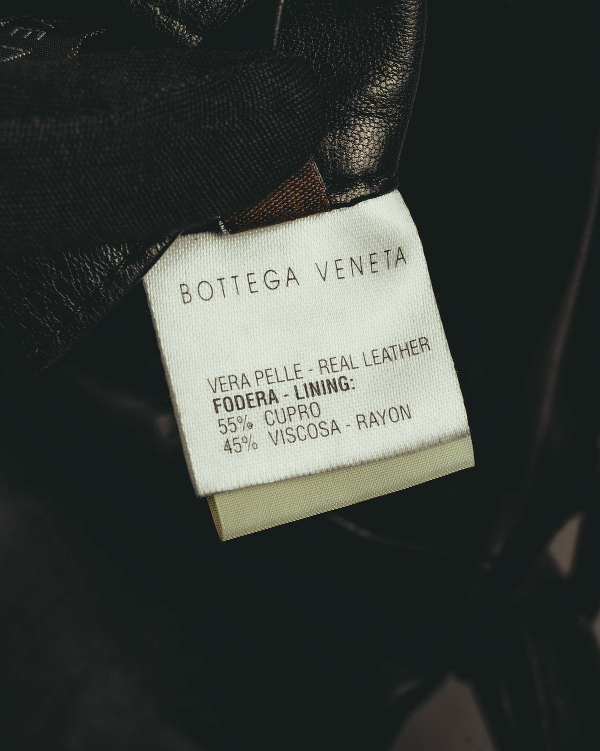 BOTTEGA VENETA 表記と、表地がリアルレザーであることを示す内タグのカット。裏地はキュプラ55パーセント、ビスコースレーヨン45パーセントと記載されています。